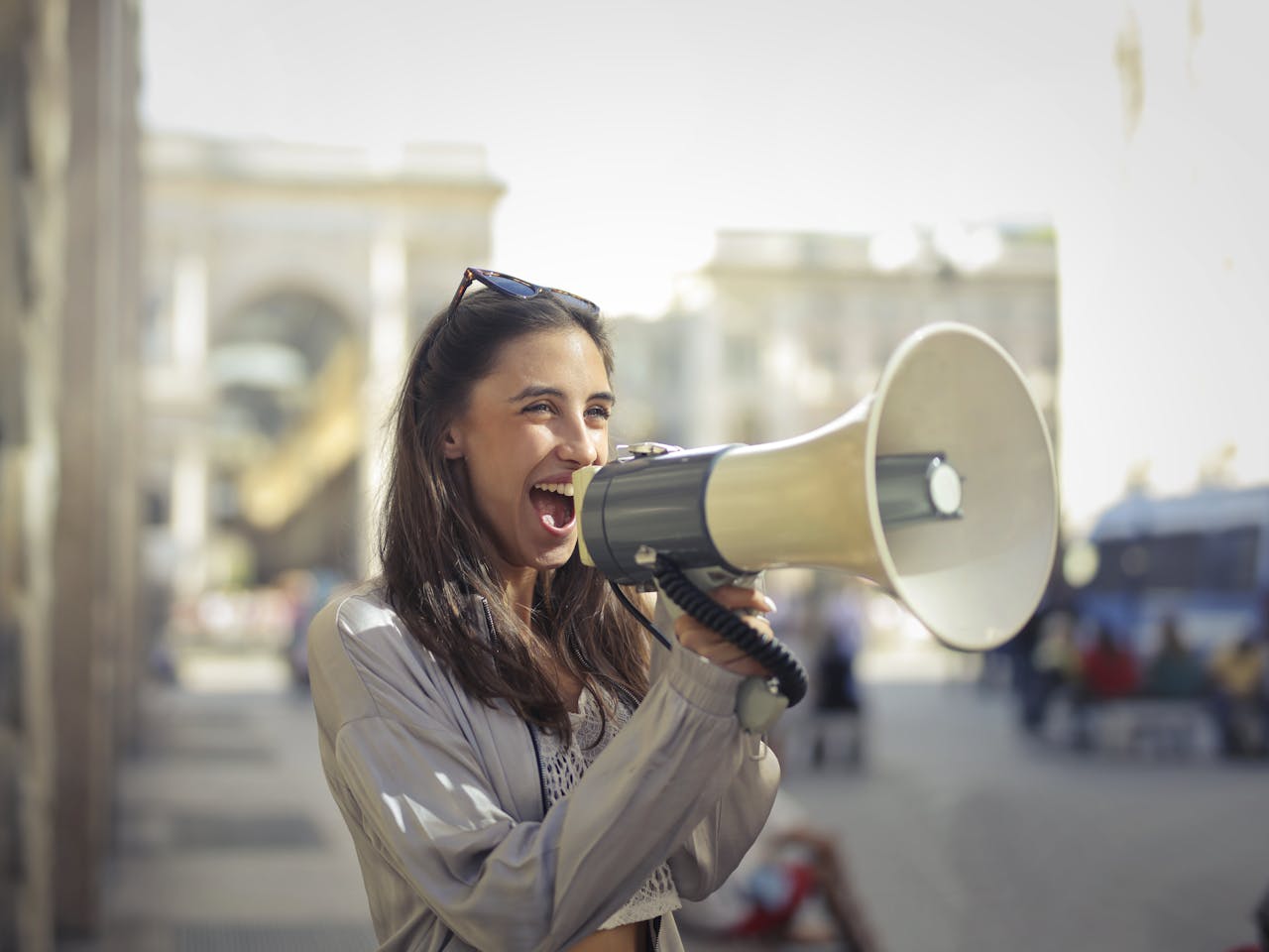 footer-02 Cheerful young woman in a casual outfit shouting into a megaphone on a sunny day.