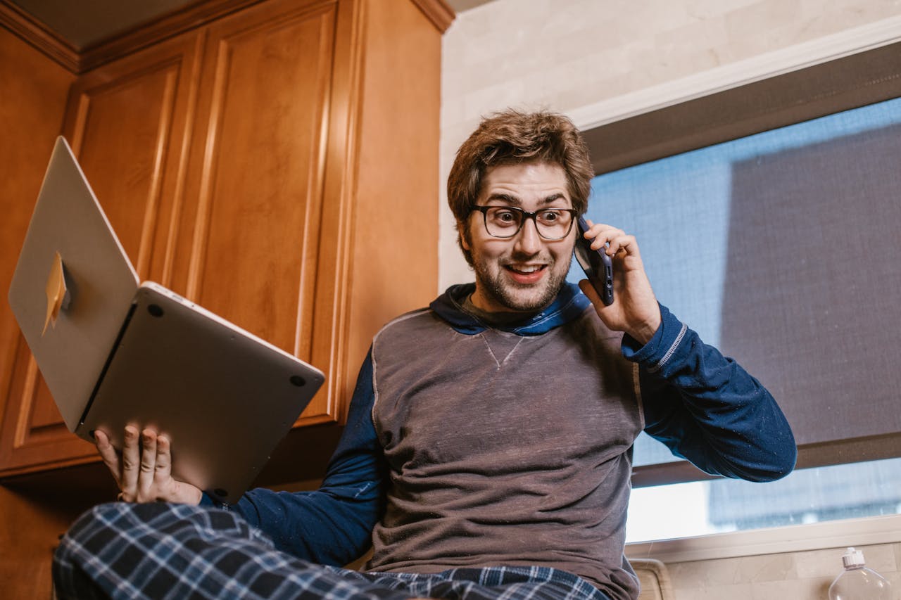 who-we-are-img Caucasian man using laptop and phone for remote work at home, relaxed and multitasking.